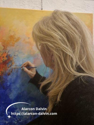 Alarcon Dalvin, artiste peintre contemporaine à Saint-Paul-de-Vence, de dos en train de peindre un tableau abstrait acrylique au couteau et pinceau, lumière provençale Côte d'Azur